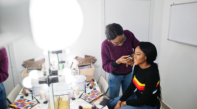 Makeup artist applying make up to a person's face - sat in beauty studio surrounded by lights and an array of makeup palettes