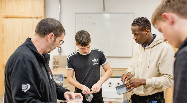 Group of students in workshop looking down working on an electrical box. Teacher stood next to group giving instructions.