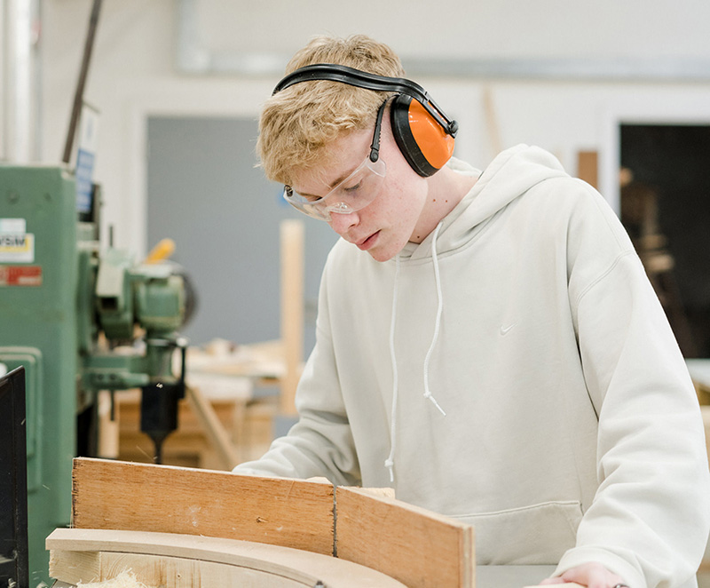 Harrogate College student wearing safety goggles and ear defenders whilst working using machinery for woodwork