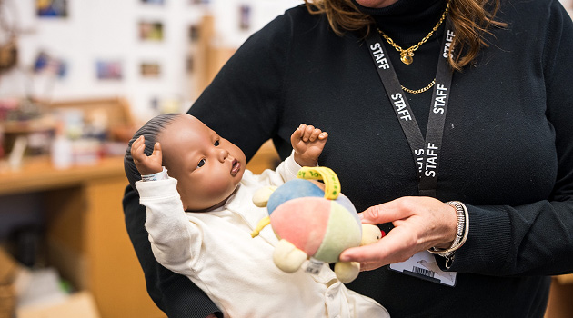 Staff member showing how to hold a baby mannequinn in arms