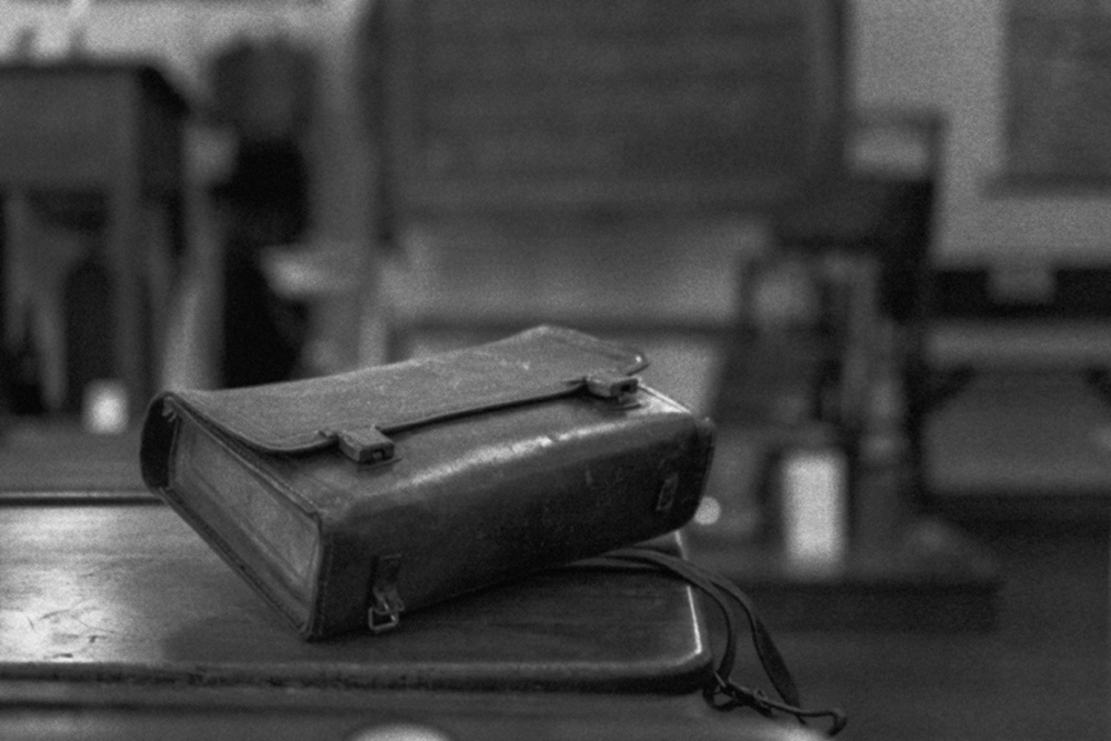 Black and white image of a vintage leather satchel on old school desk