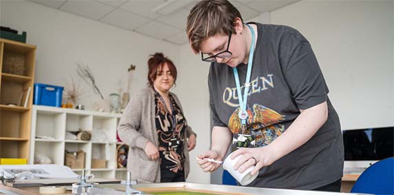 Student painting in the Creative Arts studio in Harrogate College with staff member watching on