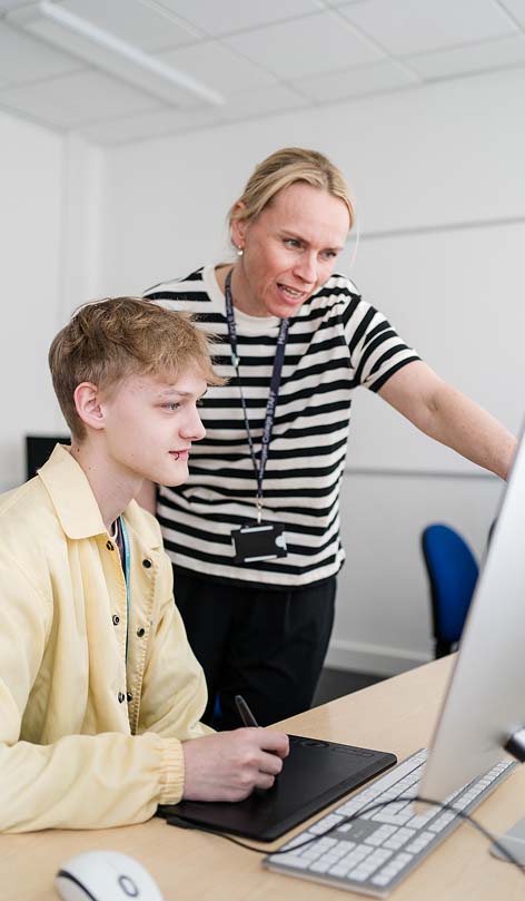 Harrogate College member of staff stood next to student sat down - helping with something on a computer