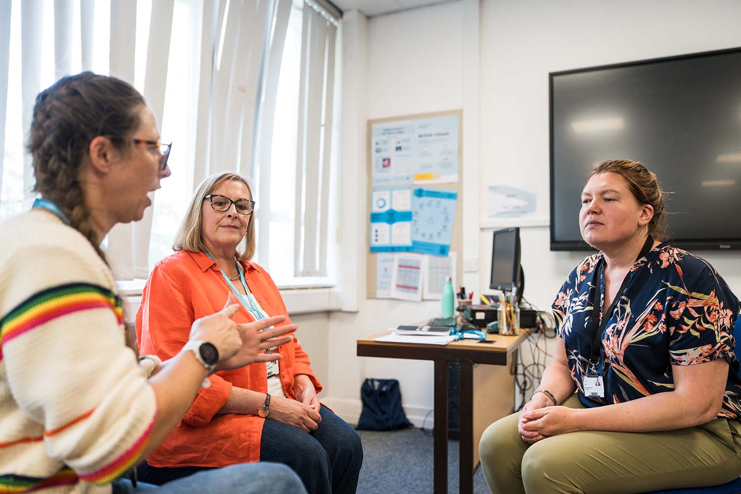 Three adults sat in classroom together in a discussion using sign language