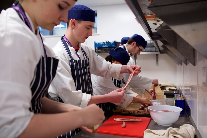 Catering students preparing strips of raw bacon for cooking