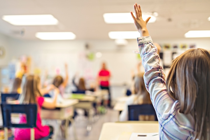 Classroom on school students in primary school raising their hands to answer the teachers question
