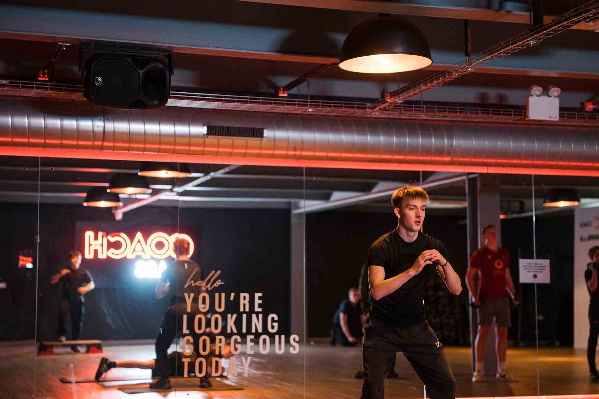 A young man in black athletic wear exercises in a modern gym studio in front of a mirrored wall.