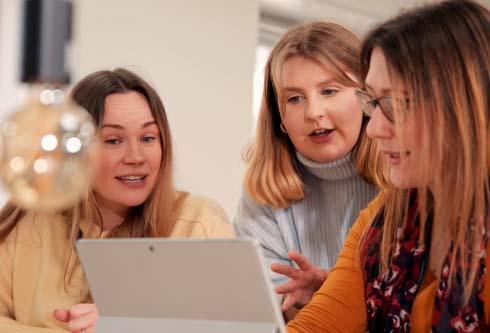 Three people sat at a desk having a discussion looking at the laptop screen