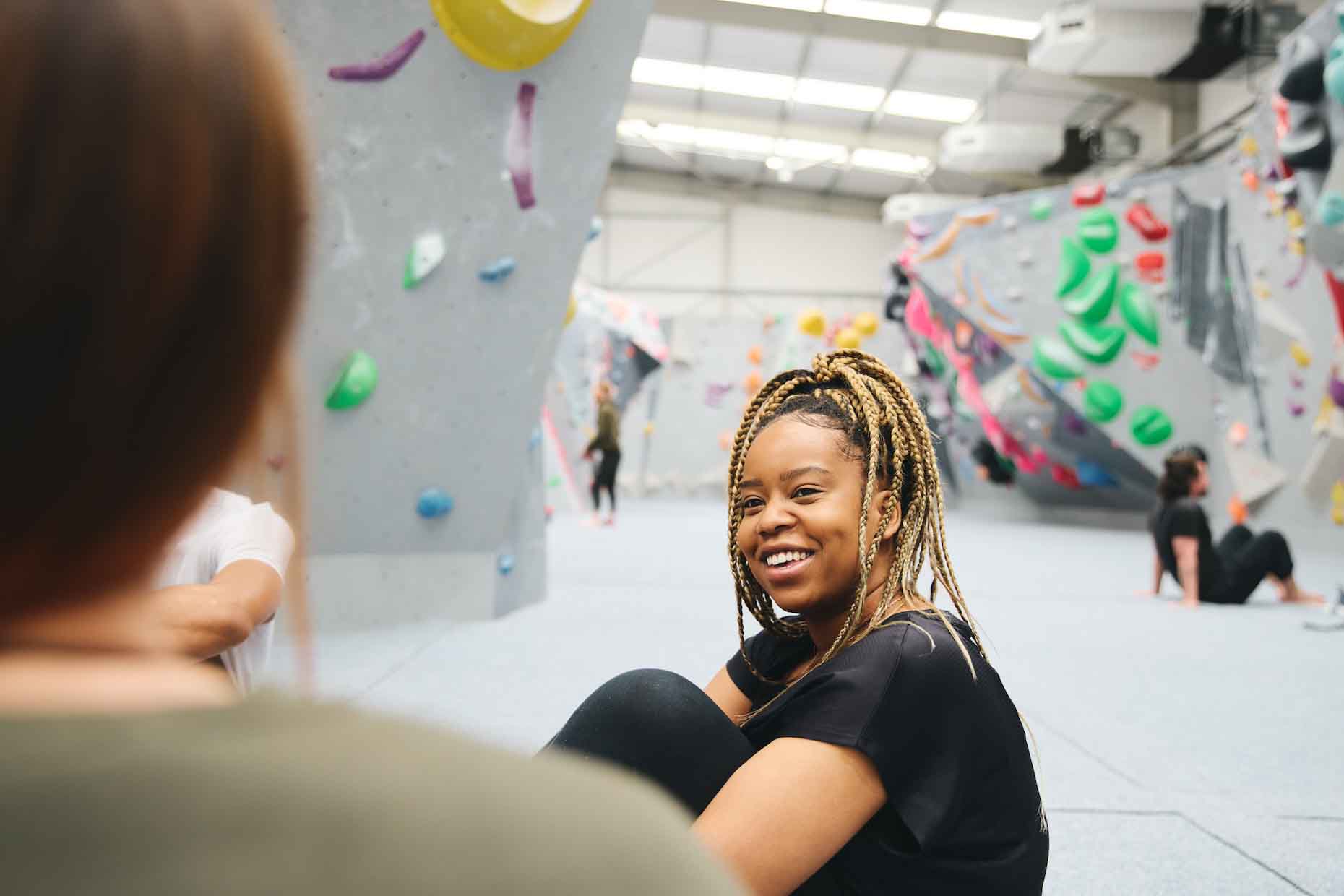 Smiling multi-cultural group of friends sitting and chatting by climbing wall in indoor activity centre