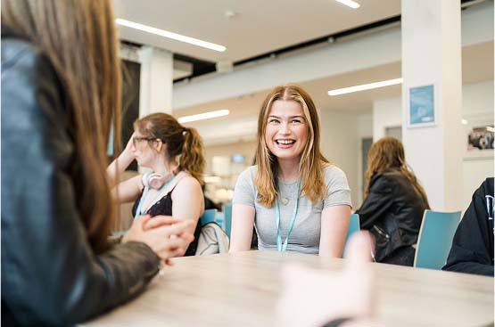 Student sat at a table in the canteen wearing a Harrogate College lanyard and smiling