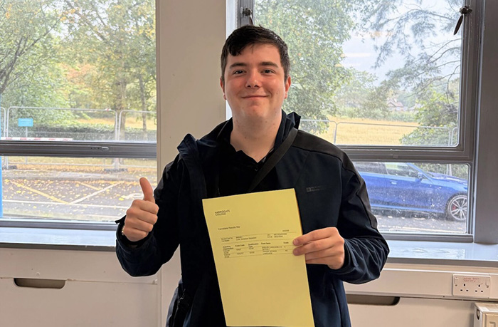 Harrogate College student Seb Luke stood holding his results certificate smiling with thumbs up